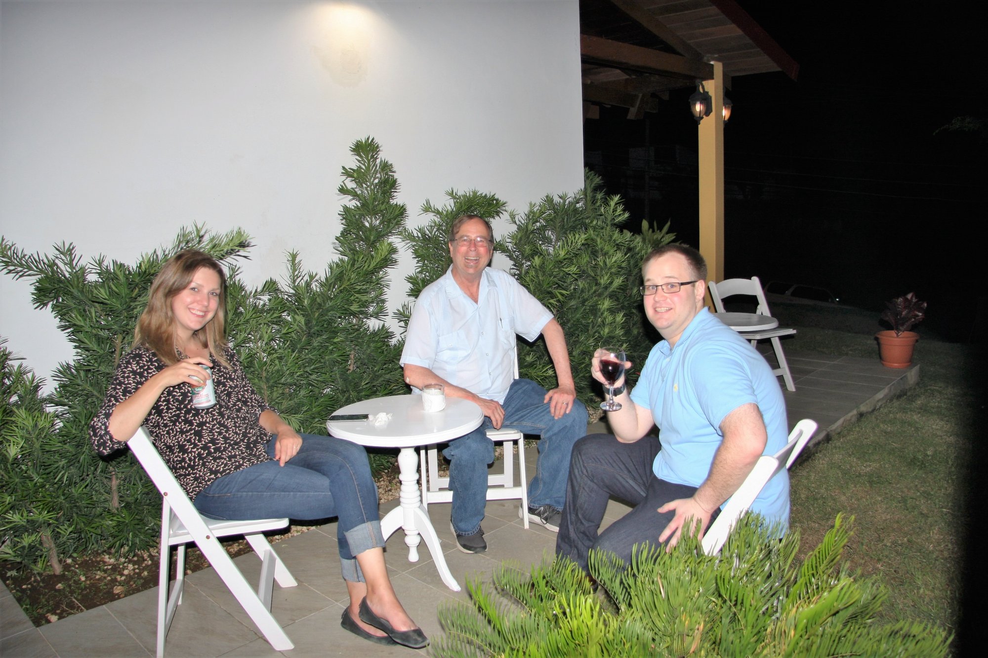Three guests relaxing with drinks at a white table in the garden at night